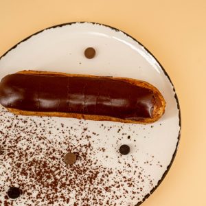 prajitura ecler asezata pe farfurie alba presarata cu cacao si boabe de cafea