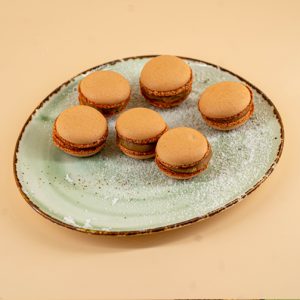 macarons caramel sarat poem caffe asezate pe o farfurie turcoaz pudrata cu zahar