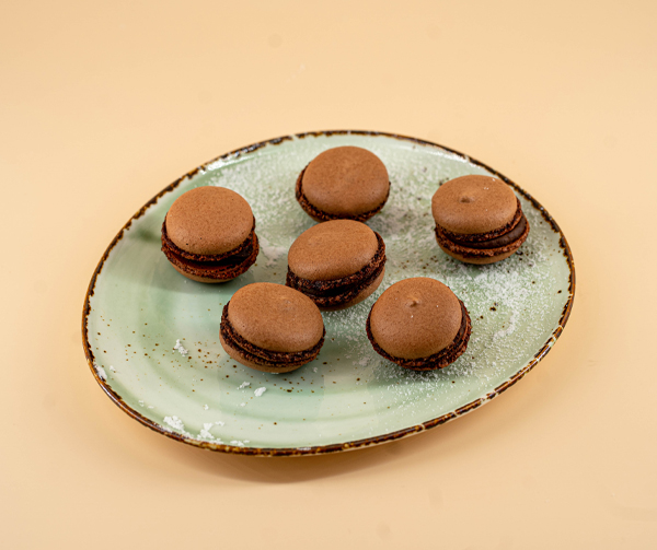 macarons ciocolata poem caffe asezate pe o farfurie turcoaz pudrata cu zahar